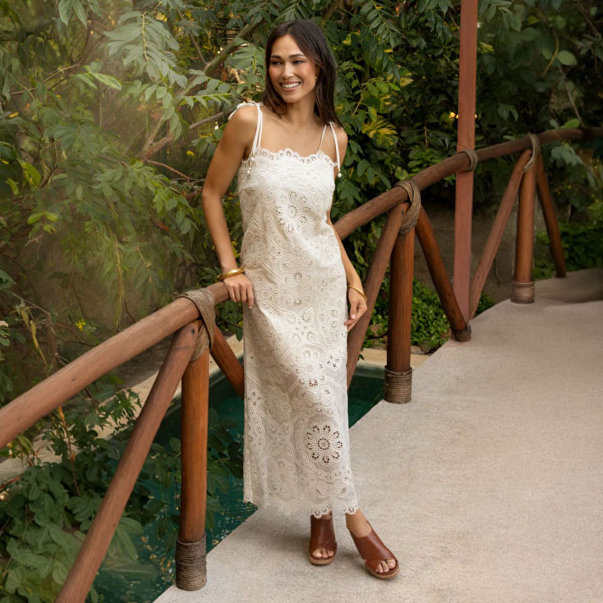 Woman standing next to a wooden fence. Featuring the Liv sandal in brown. 