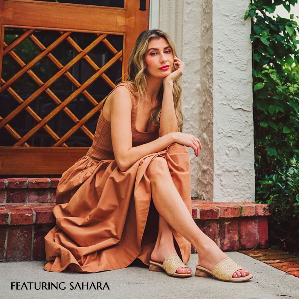 Model sitting on brick steps featuring the Sahara sandal in tan.