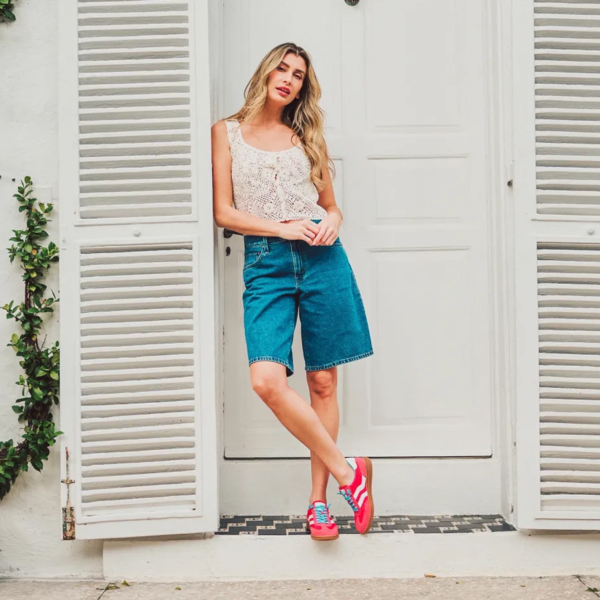 Woman leaning against a white door wearing the Remmi lace-up sneaker in pink.