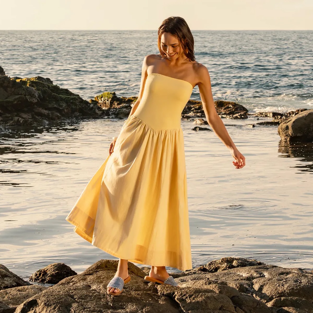 Woman standing on rocks on a beach wearing the Elsa slide sandal in Blue.