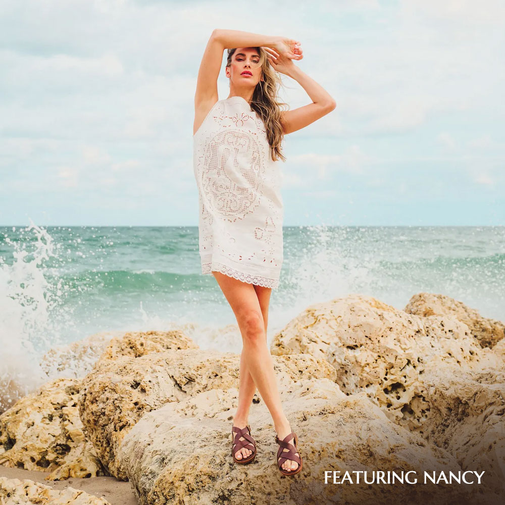 Model standing on rocks by the ocean featuring the Nancy sandal in brown.